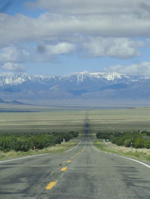 A lonely Nevada road: long, straight, silent, and empty, leading towards the snowcapped mountains in the West.
