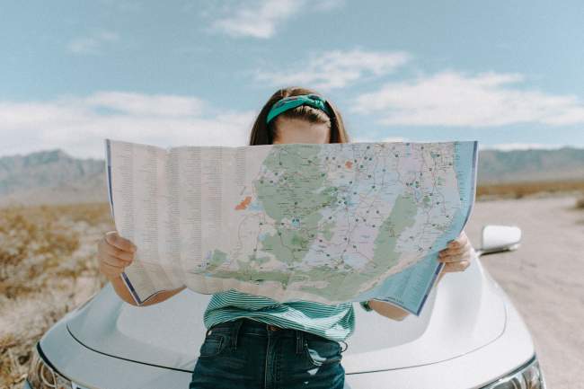 Girl looking at a map leaning against a white car in the desert